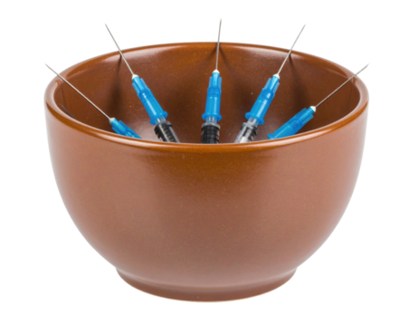A brown bowl contains six blue and black syringes with needles pointing upwards.
