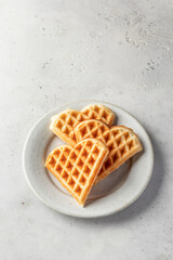 Heart shaped waffles on white ceramic plate isolated on gray background
