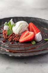 Dessert whith scoop of ice cream, strawberries, biscuit crumbs, chocolate and berry sauses on black plate. Fancy restaurant serving
