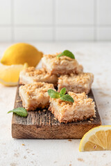 Lemon crumble bars on wooden cutting board on white tile background. Oatmeal lemon bars