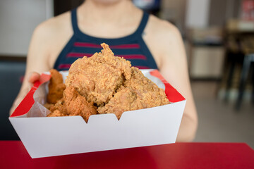 Close-up of a woman holding a box of fried chicken inside a restaurant