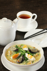 A hearty bowl of Chinese spinach soup with three kinds of eggs (salted egg, century egg, and regular egg) is presented on a dark wooden table 
