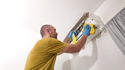 Man cleaning and maintaining air condition unit at home.