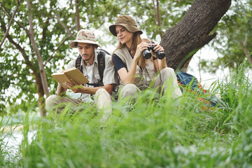 Bird watching is recreational pursuit. Multiracial woman and friend have fun outdoors leisure activity looking up for bird in nature park. Diverse people enjoy using binocular for bird watch adventure