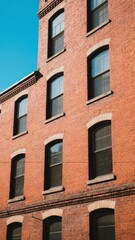 Obraz premium Red Brick Building with Symmetrical Windows Against a Clear Blue Sky