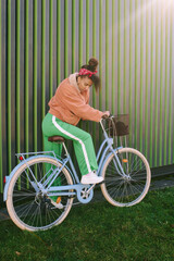 Outdoor fashion portrait of pretty african woman sitting on bike, leaning on the wall