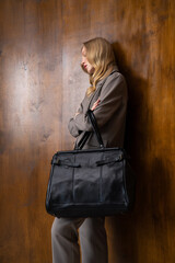 A stylish young woman, long blonde hair, poses in a grey suit, holding a black leather bag against...
