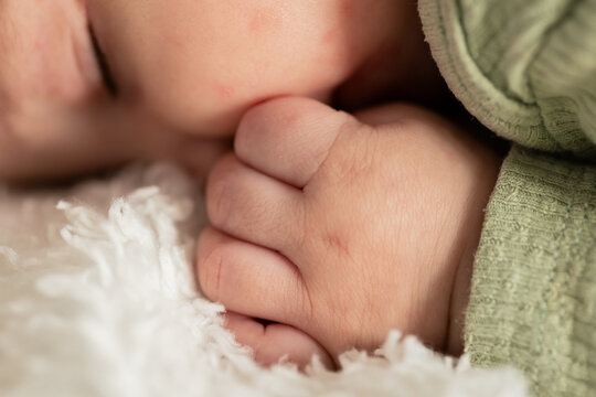 Female infant sucking thumb, resting on plush white blanket in crib wearing green ribbed sleeper