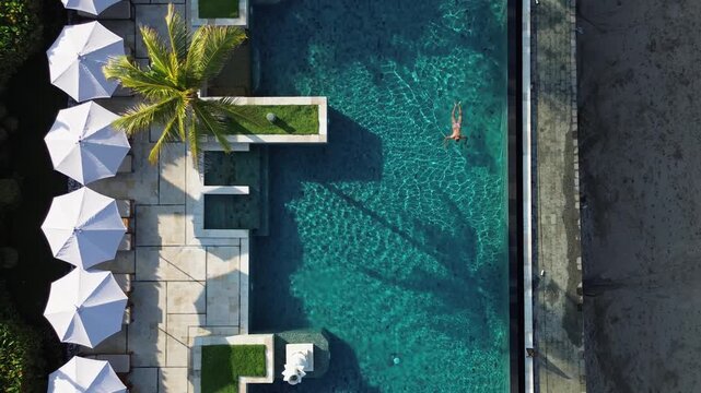 Aerial view of young woman swimming in infinity pool under the palm trees at sunny day.Bali.Indonesia