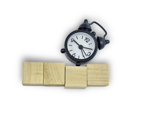 Black alarm clock perched atop balanced wooden blocks, isolated on white.