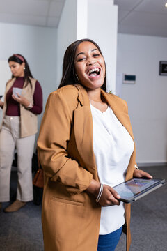 Diverse female colleagues laughing while checking smartphone and holding tablet in modern office