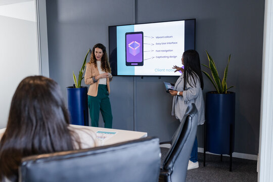 Diverse coworkers presenting app interface in conference room using tablet and reviewing documents