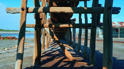 Abandoned wooden structure on the ocean coast. Old winch rusty from salt water. Dead zone. Wooden structure for transporting salt from the mine. Old brown poles against the blue sky.