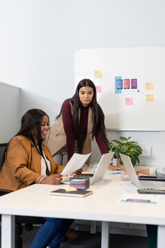 Diverse female coworkers reviewing documents in office meeting using laptops and sticky notes