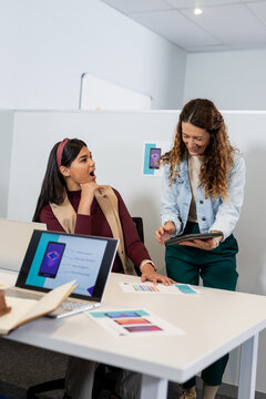 Diverse coworkers collaborating over laptop and tablet at office cubicle with color swatch charts
