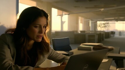 Professional working late in empty office space while using laptop at sunset, creating atmospheric corporate environment for business and technology concept