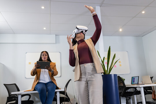 Diverse female colleagues demonstrating virtual reality in office with VR headset and tablet