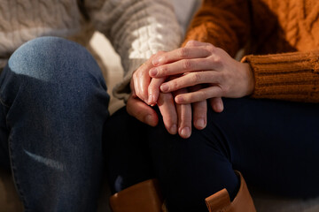 Couple sitting on sofa holding hands gently on lap in living room wearing cable knit sweaters