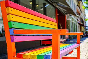 Brightly colored bench on a stone pavement with vibrant rainbow stripes, showcasing creativity and public art in a sunny urban setting