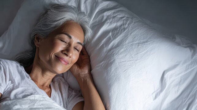 Senior asian woman resting peacefully, lying comfortably in bed with soft smile, demonstrating serene nighttime sleeping experience and wellness