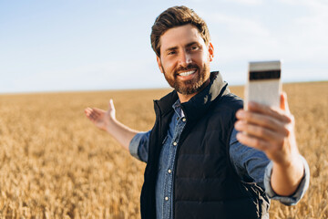 Happy farmer taking selfie and showing wheat field with mobile phone