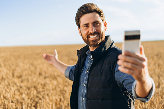 Happy farmer taking selfie and showing wheat field with mobile phone