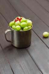 Metal mug with green gooseberries and red currants on top.