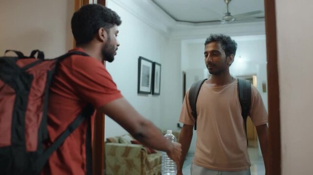 Friendly Farewell: Two young men greet each other at a doorway. One is preparing to leave with a backpack. The other is welcoming at home
