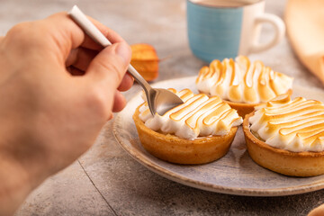 French lemon tart with meringue with hand on brown concrete, orange linen textile, side view, close up, selective focus