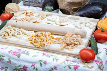 A wooden cutting board with various pasta and vegetables