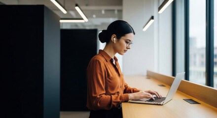 Serious young businesswoman working efficiently on a laptop in a sleek, minimalist, and contemporary office environment with natural lighting.