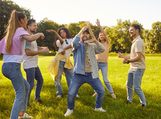 Portrait of a group of excited happy young people friends having fun hanging together in nature in the park. Happy students in casual clothes dancing outdoors on a sunny summer day on a weekend.