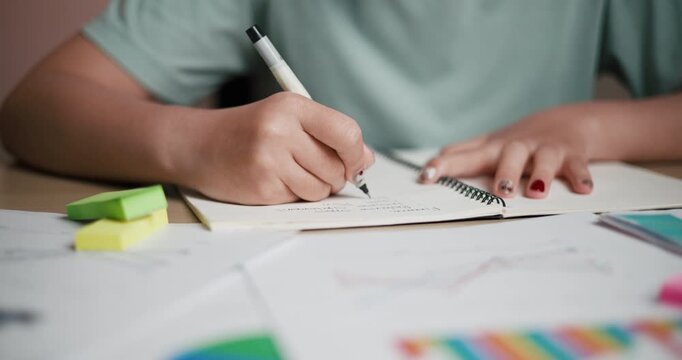 Handheld selective focus shot, A woman is taking notes in a notebook while sitting at a desk filled with business charts and sticky notes.