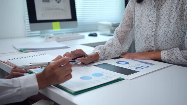 Experienced businesswomen collaborating while analyzing financial charts and graphs, discussing company performance during professional office meeting, pointing at data visualizations