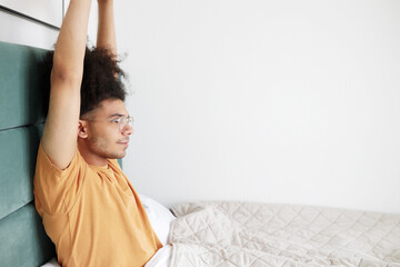 Sun salutation in bed. Side view of handsome guy tourist of african ethnicity in glasses stretching...