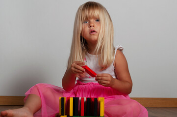 blonde blue-eyed girl, 4 years old, playing with a construction set at home