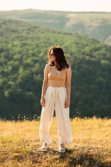 A woman dressed in light, flowing clothing stands gracefully amid a grassy field, encircled by lush...