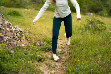 Woman spraining ankle while running outdoors, wearing sportswear and white sneakers, foot twisting on uneven grass surface in mountains, risk of sports injury and leg trauma during outdoor activity