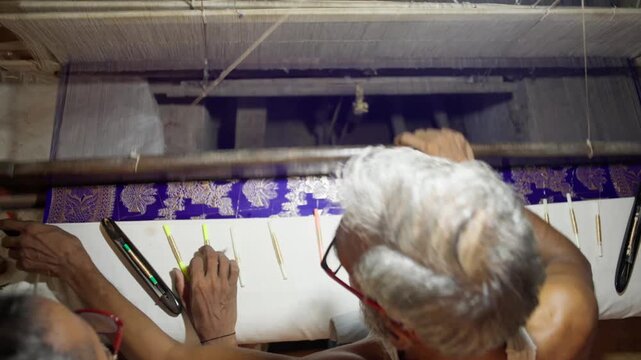 Top view of artisan weaving intricate Banarasi silk fabric using handloom tools in Varanasi, India. Detailed textile work in traditional craftsmanship.