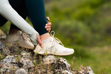 Close-up of woman in sportswear holding ankle in pain after outdoor workout, injury or muscle strain during fitness activity in nature, consequences of overtraining concept