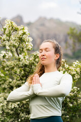 Meditation in nature. Portrait of calm young woman meditating in spring mountains, holding her hands in namaste gesture, wearing long sleeve, outdoor yoga activities, mindfulness lifestyle