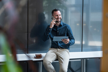 Smiling manager using tablet and phone in modern office setting