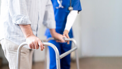 Cropped shot of young nurse helping old elderly disable man to walk using walker equipment at home
