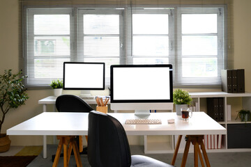 Home office interior with desktop computers on white desks and natural light from large windows