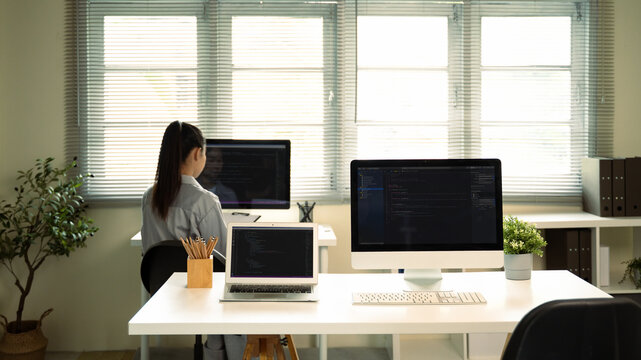 Female software developer focuses on writing code on monitor in a bright workspace - Powered by Adobe
