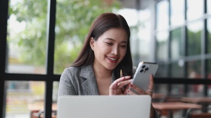 Beautiful asian businesswoman working with smartphone and laptop while sitting at cafe, smiling female freelancer enjoying online work in coffee shop - Powered by Adobe