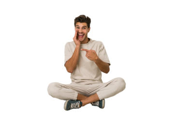 Young caucasian man sitting on the floor isolated on white background saying a gossip, pointing to side reporting something.