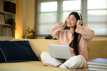 Naklejka premium Cheerful teenage girl enjoying music on headphones with laptop on lap