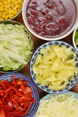An overhead flat lay showcases a vibrant array of fresh, colorful chopped salad ingredients, including corn, kidney beans, shredded lettuce, red and yellow bell peppers, and cheese, presented in vario