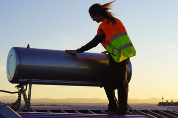 Renewable Energies. Technical Woman Installing Solar Panels and Placing Hot Water Tank on Roof